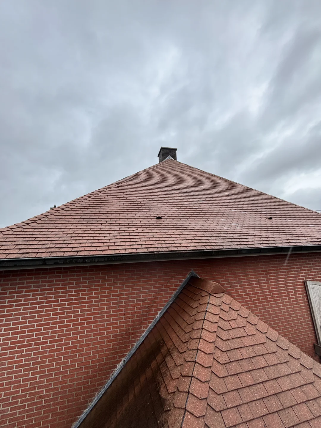 Dakreiniging pannendak - Renovivo West & Oost-Vlaanderen Schoon pannendak met rode dakpannen en schoorsteen, klaar voor professionele dakreiniging en algbehandeling door Renovivo.