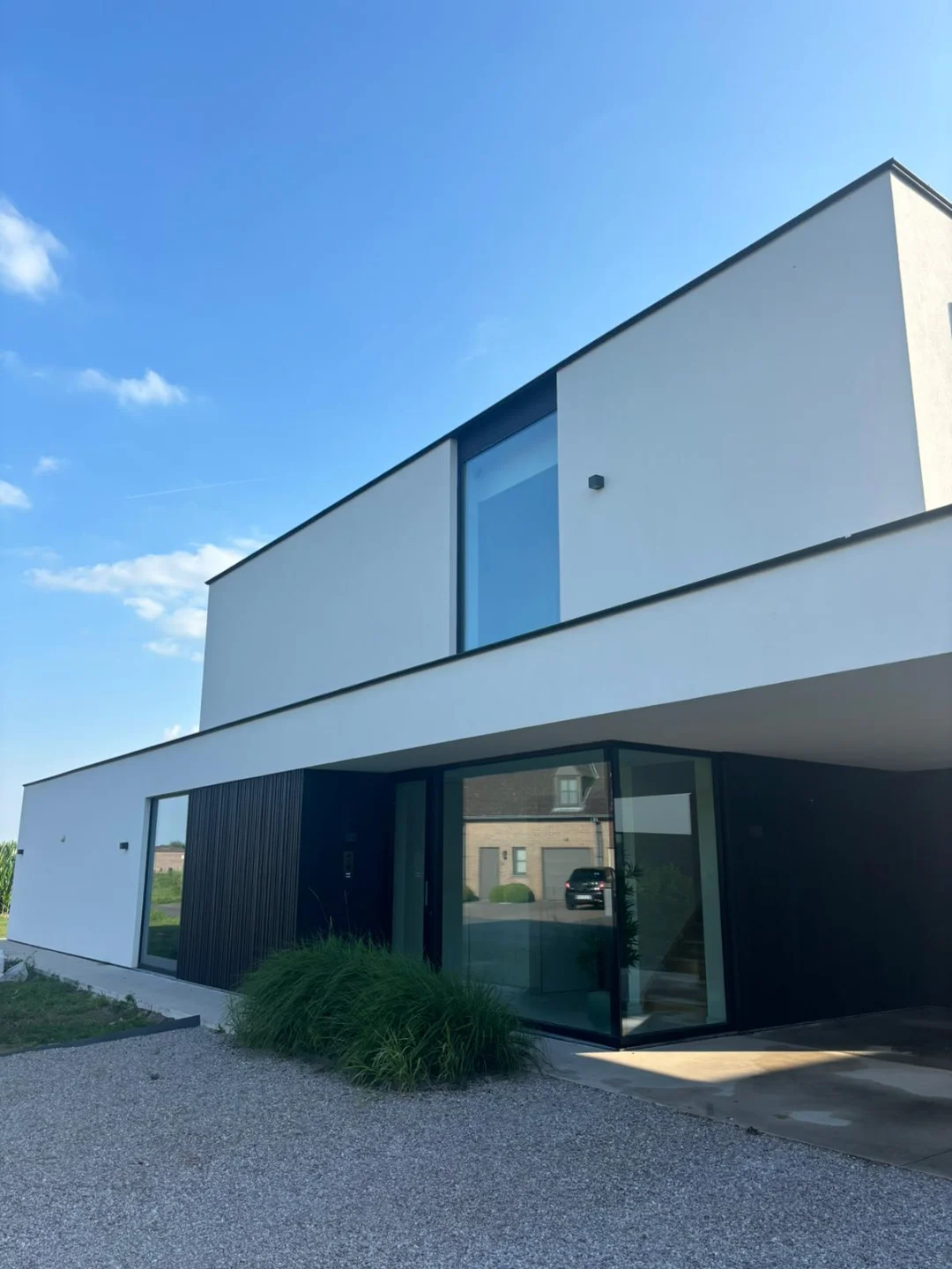 Strakke gevel en schone ramen dankzij Renovivo reiniging Een stralend schone moderne woning met witte gevels en grote spiegelende ramen, ideaal voor Renovivo's gevel- en ramenreiniging.