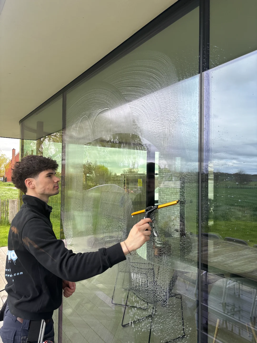 Renovivo: Ramen Wassen in West & Oost-Vlaanderen Professionele glazenwasser van Renovivo wast grote ramen van een modern pand in West- of Oost-Vlaanderen.