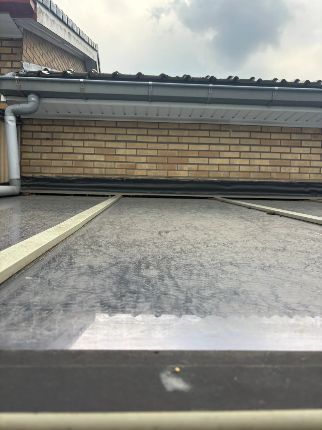 Renovivo: Professionele reiniging van zonnepanelen, dak en gevel Detailfoto van vuile zonnepanelen met een vieze dakgoot, dakrand en bakstenen gevel. Renovivo reinigt in West & Oost-Vlaanderen.